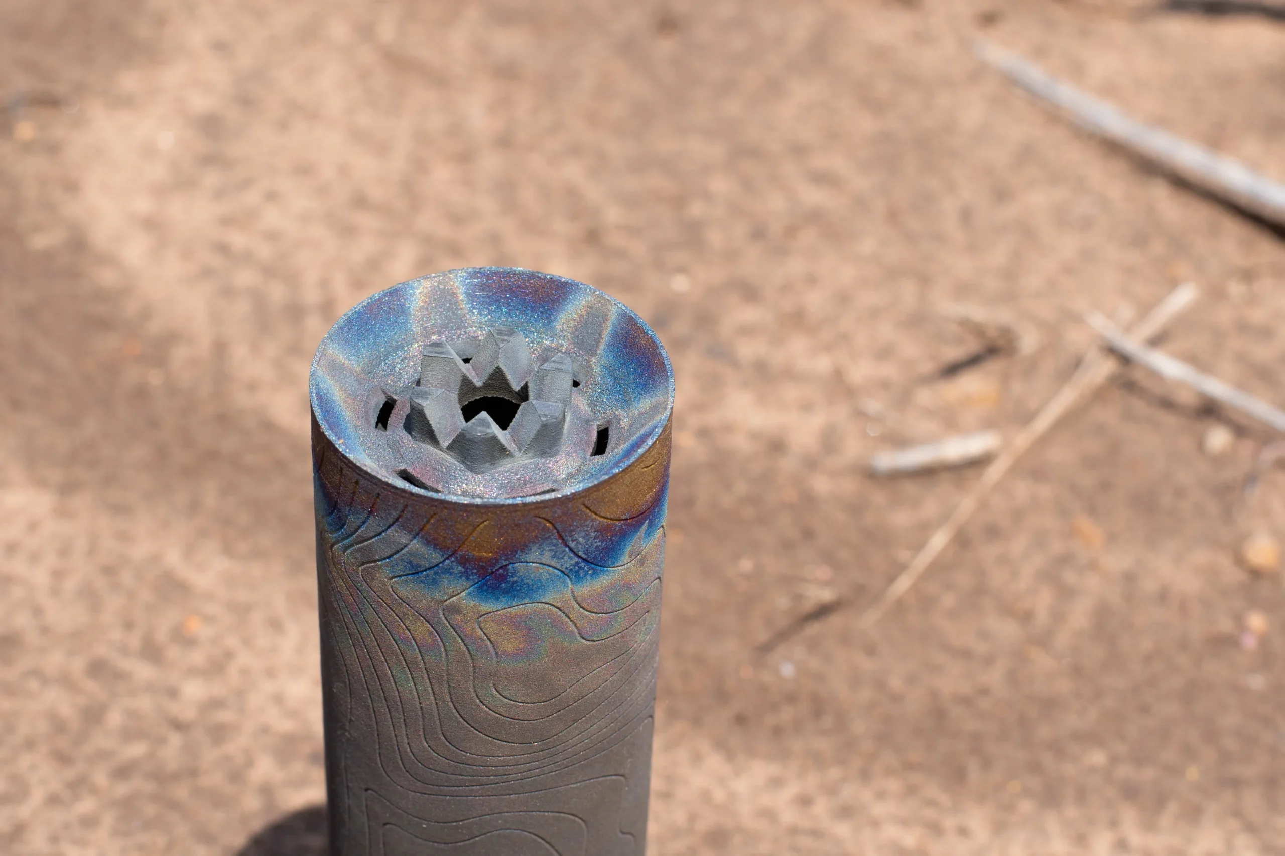 Heat colored titanium suppressor standing upright, muzzle end showing the raw print texture and internal baffle